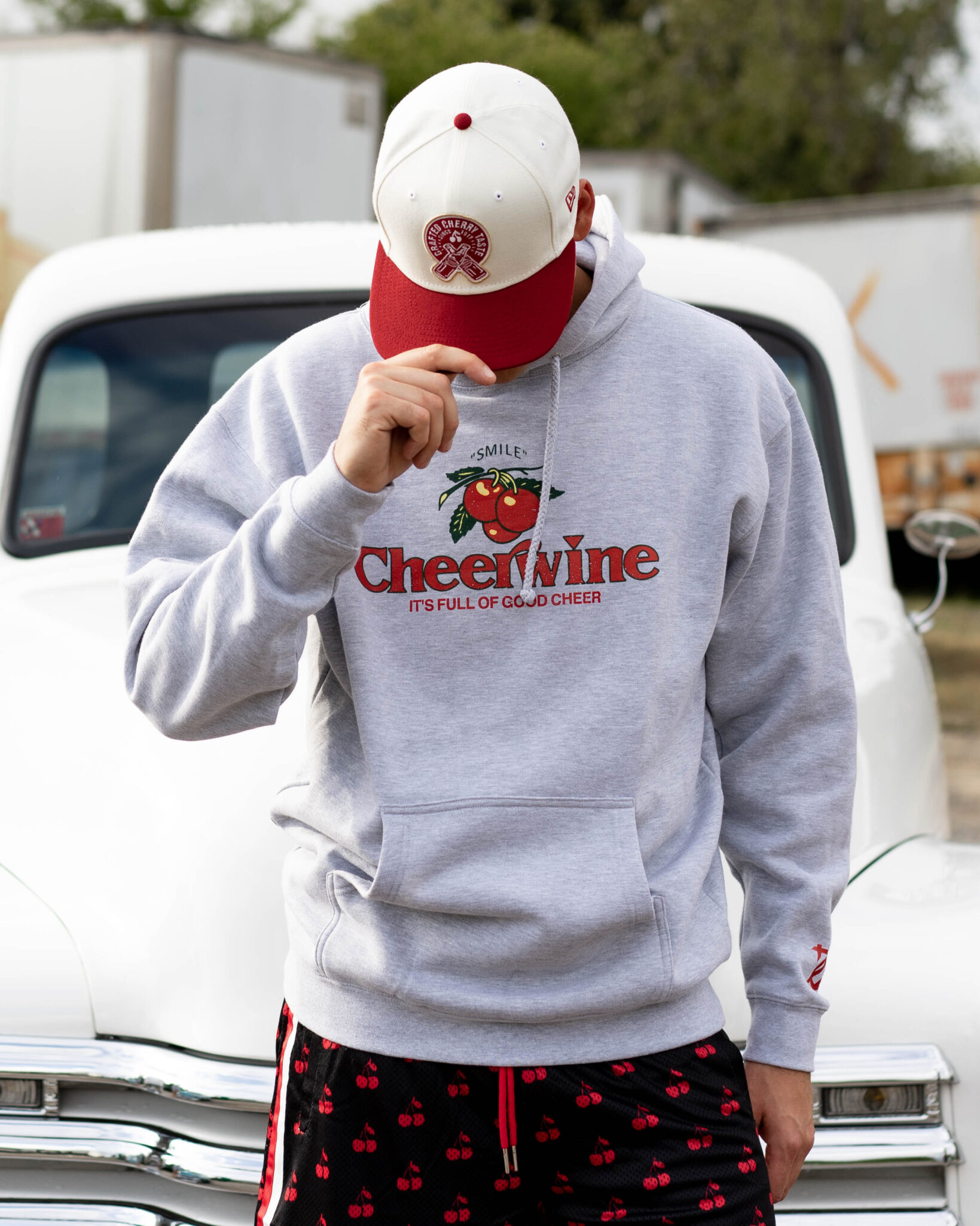 Person in Cheerwine hoodie and cap stands in front of classic truck.