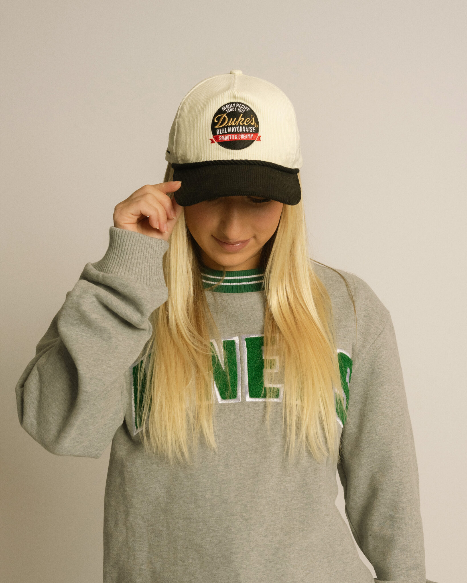 Woman wearing a Duke's mayonnaise cap and a gray sweater.